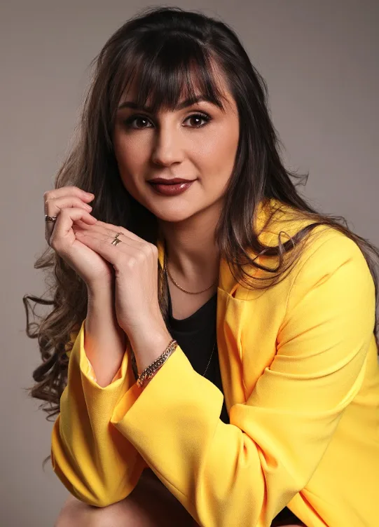 Dra. Laís Fracasso sorrindo, com blazer amarelo e mãos unidas